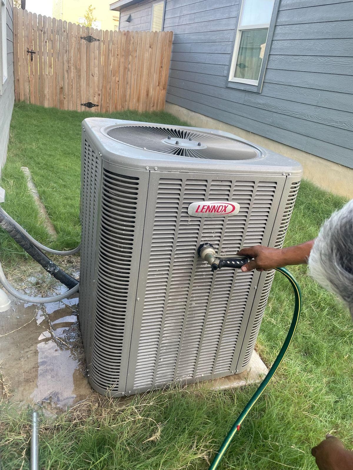 AC American Air technician cleaning Lennox outdoor condenser unit during maintenance service in San Antonio